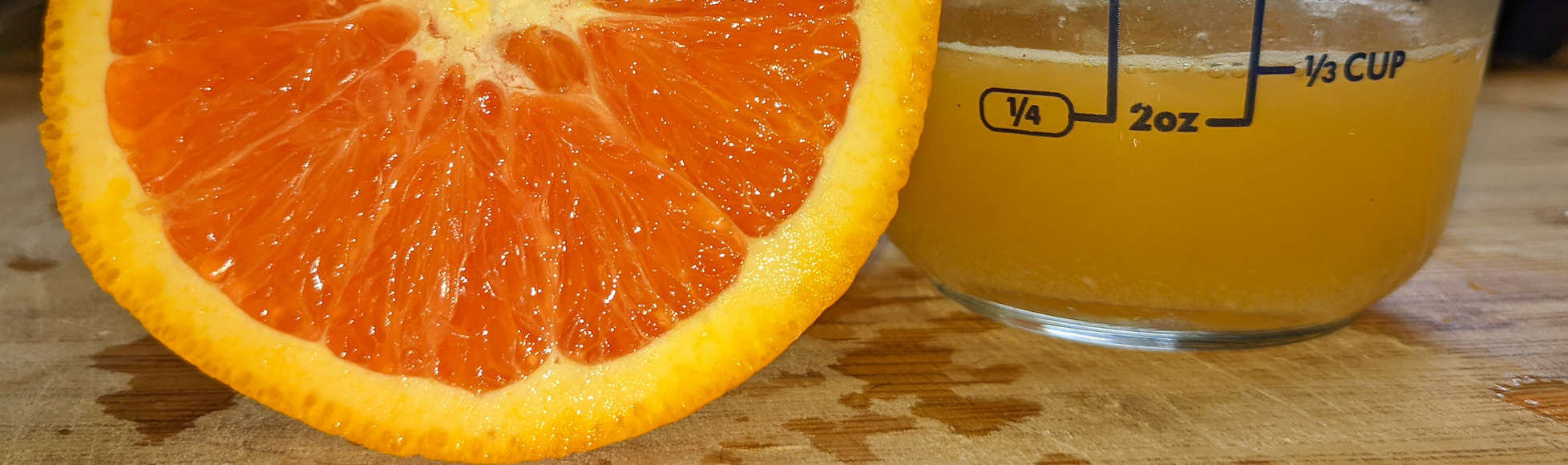 close up of cut orange next to orange juice in measuring cup